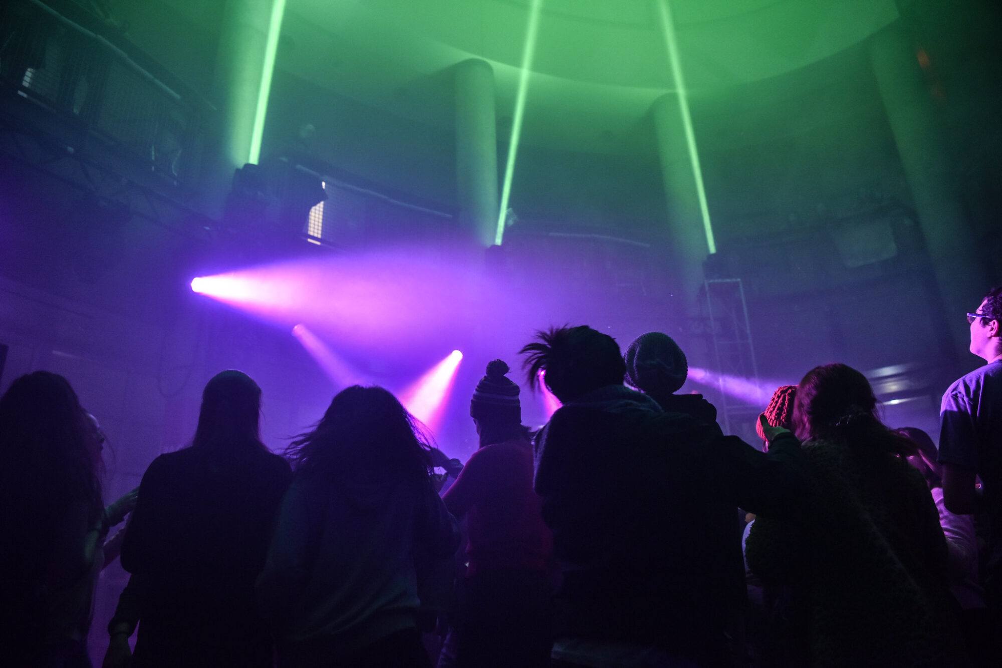 A group of students in a dark lobby watching a light show; the lighting effects are green and purple spotlights pointing in all directions.