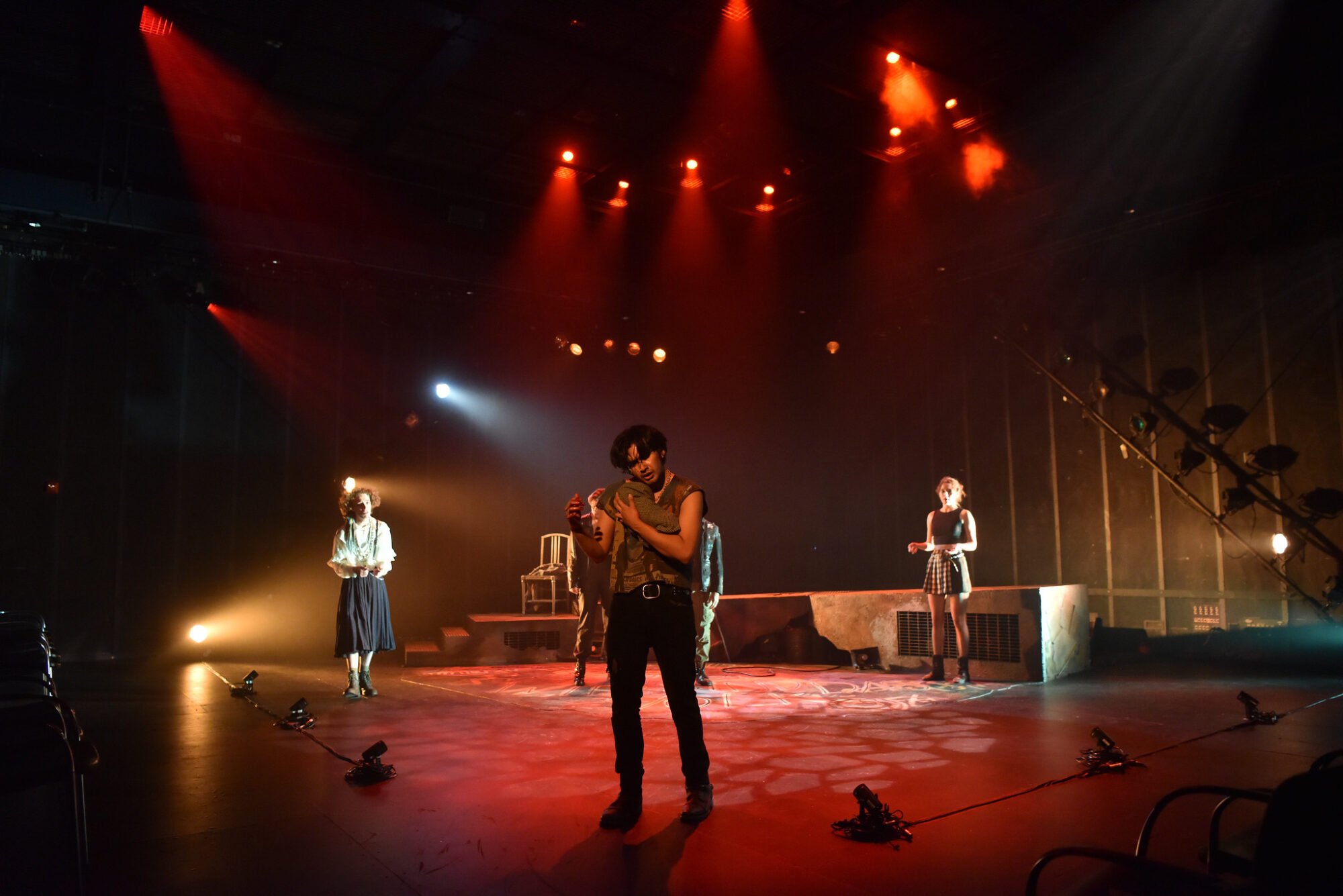 Actors on stage with dramatic red spotlights illuminating the space.