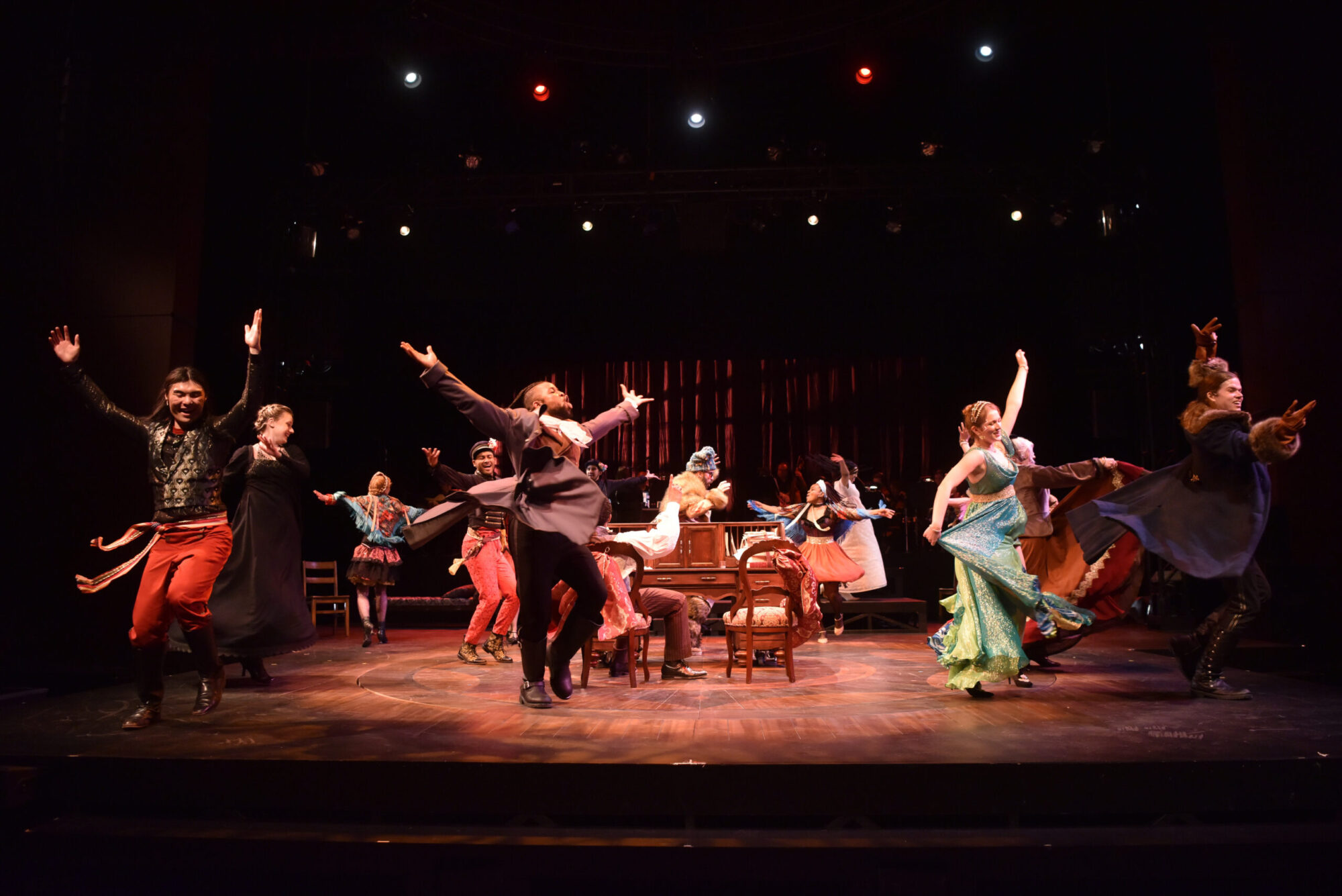 A stage full of students in costumes, arms stretched out, turning and dancing, as part of a production of "Natasha, Pierre & the Great Comet of 1812."