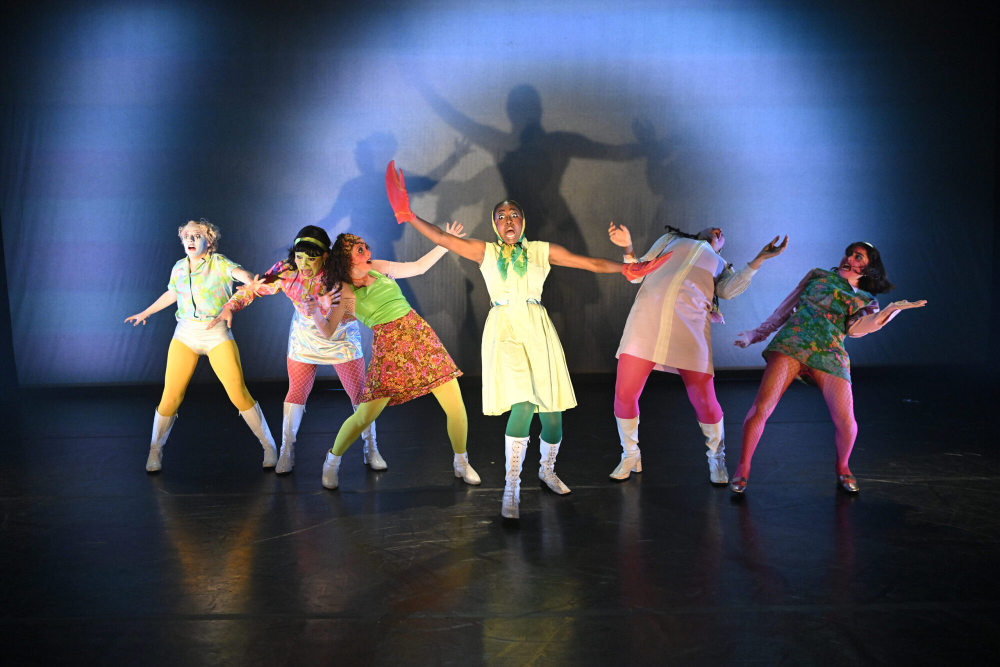 Six students I brightly colored costumes dance, bending backwards, with extreme facial expressions; the student center stage has a lobster claw on her hand.