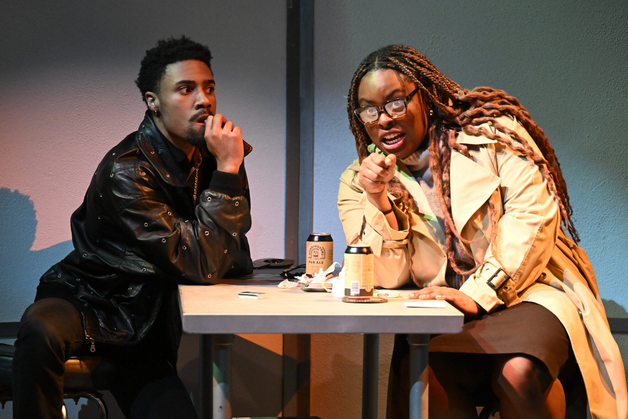 Two students sit at a table on stage, acting out a scene from "Love and Money."