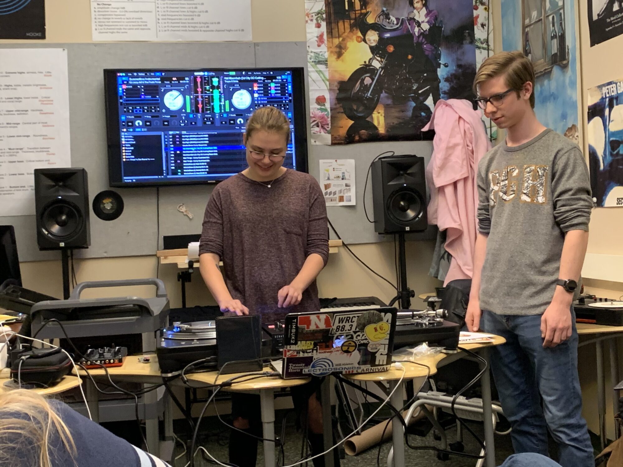 Two students standing in a classroom, working on equipment for a DJ set up.