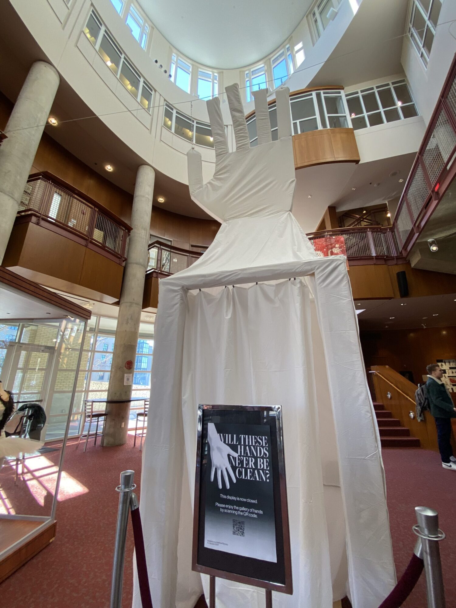 A large display of a hand, covered in a white sheet in the lobby of the Purnell Center for the Arts, a sign in front of it reads: “Will these hands ne’er be clean?”