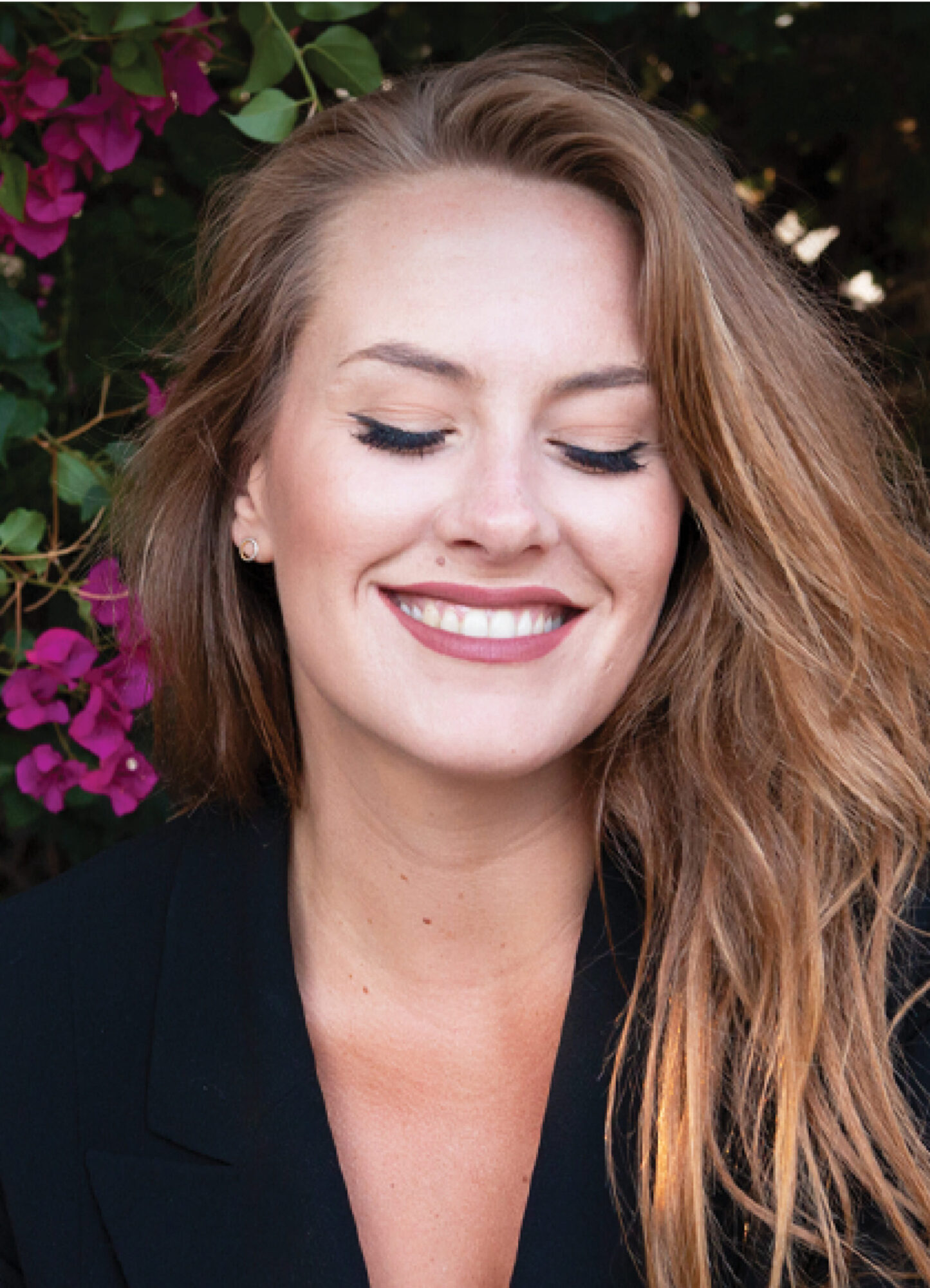 Mary-Margaret Kunze smiles, eyes closed, with pink flowers behind her.