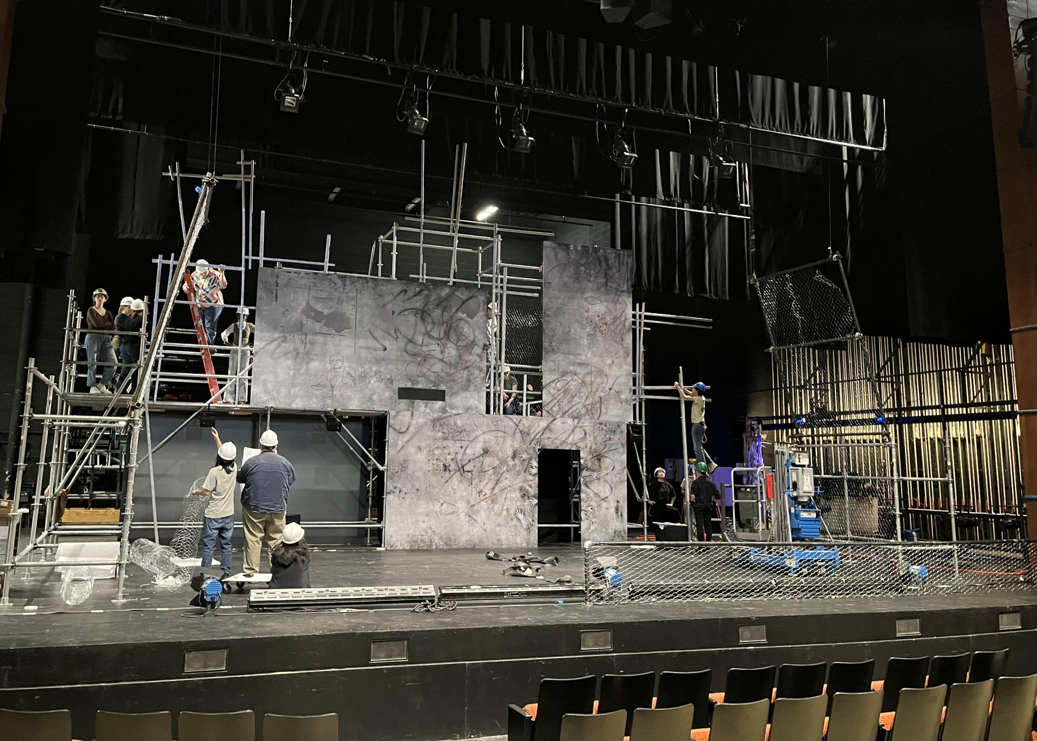 A group of students work on a large set load-in on the stage of the Philip Chosky Theater.