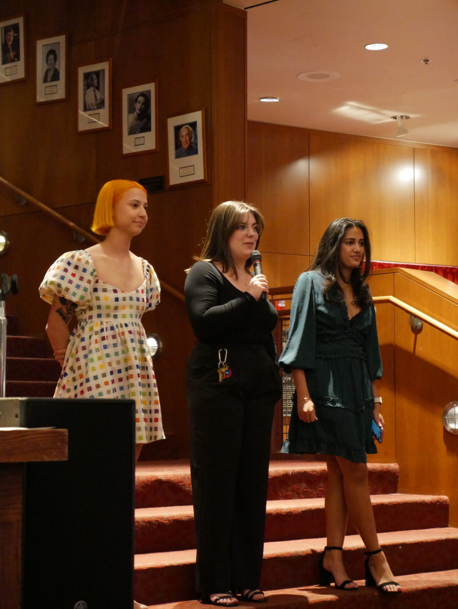 Three students, wearing dresses, stand on a staircase in the lobby of the Purnell Center for the Arts.