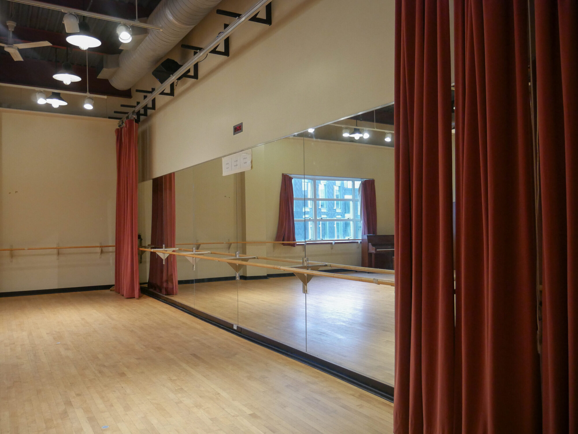 A photo of the Brown Movement Studio, with light wood floors, a wall of mirrors, a ballet bar, and red curtains hanging on the sides.