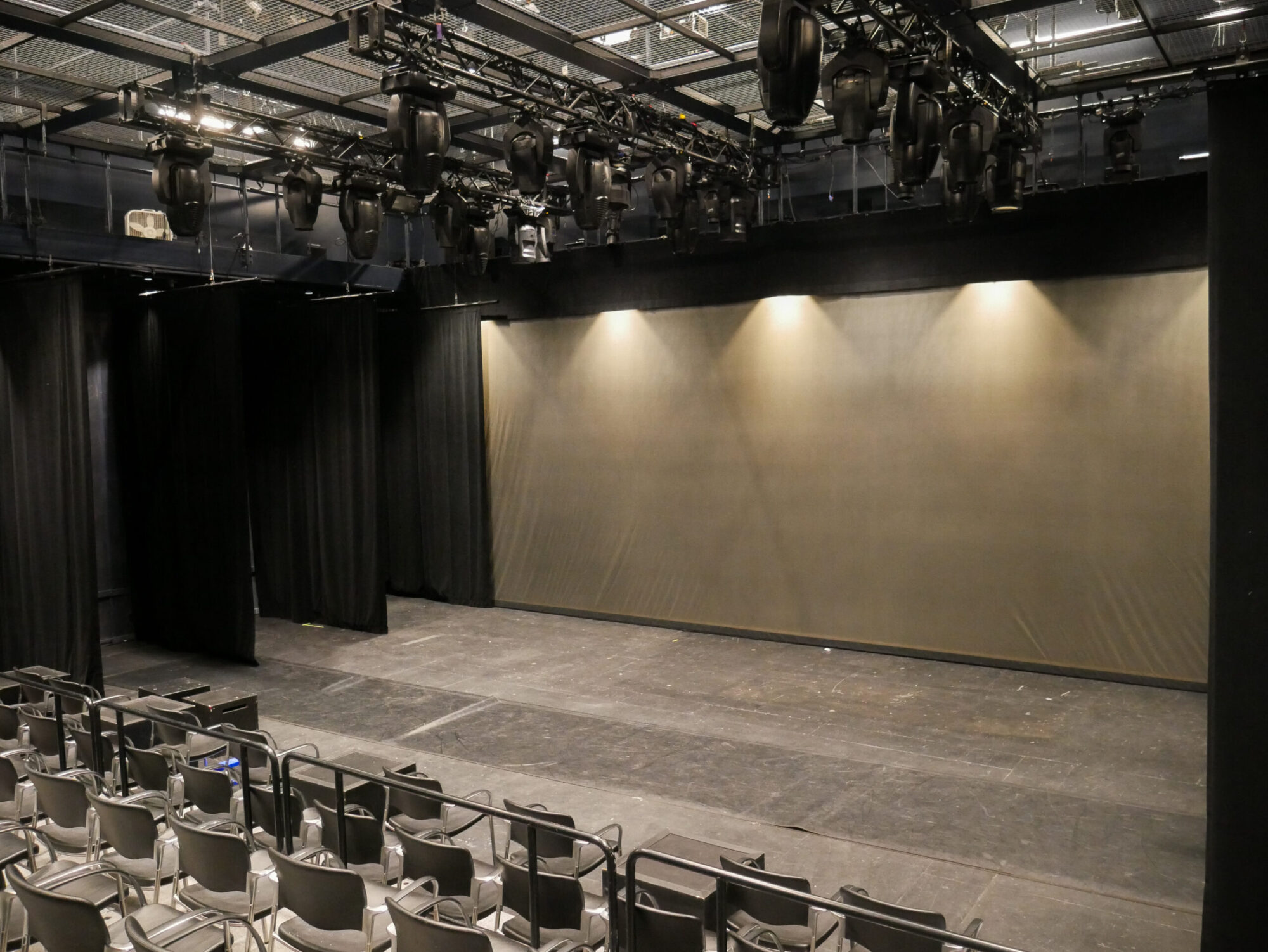 Photo of the interior of the Helen Wayne Rauh block box theater - an empty stage with seating and overhead lighting shining down.