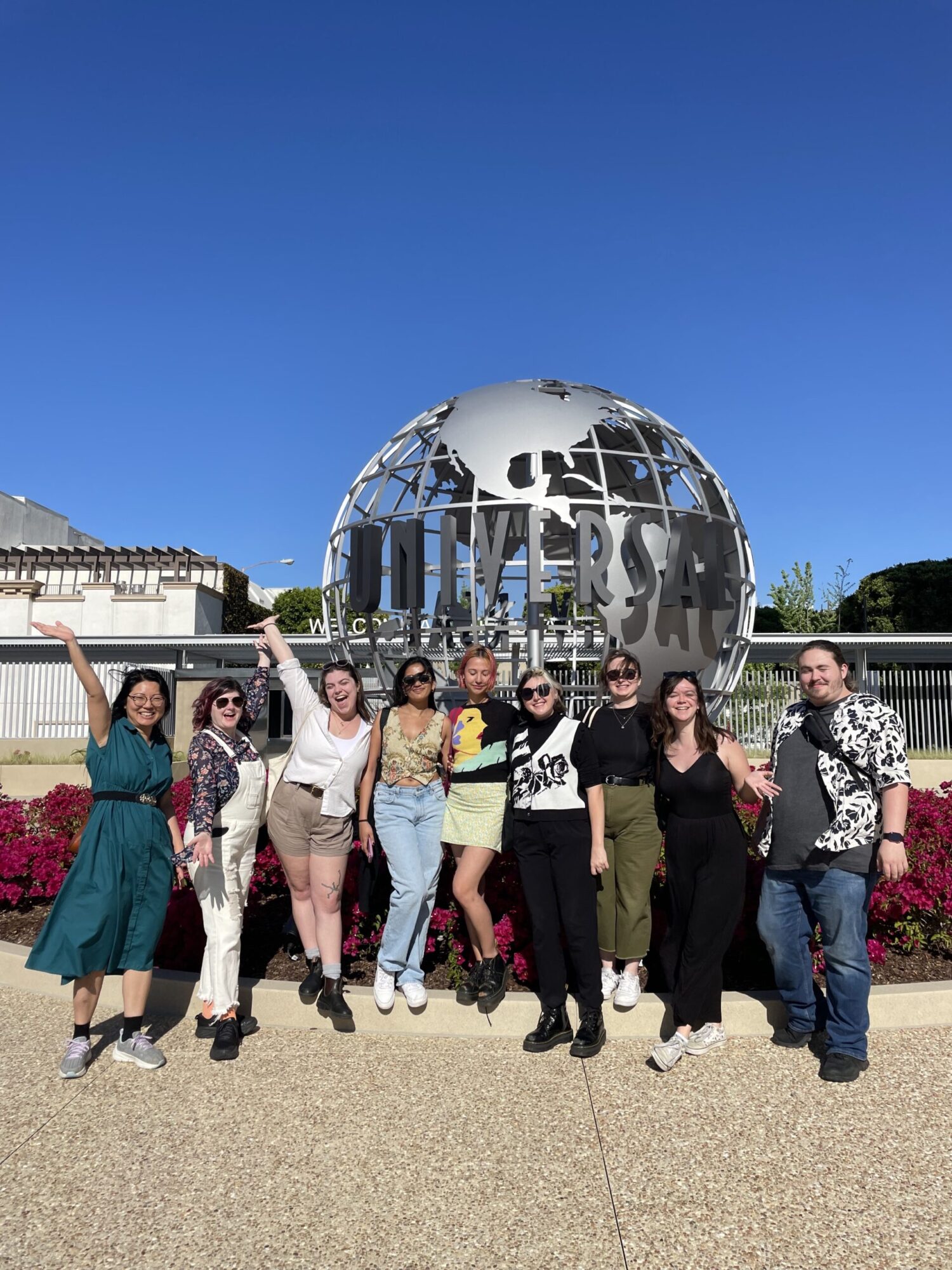 A group of students pose with arms out and big smiles, in front of the Universal Studios globe statue in Los Angeles.