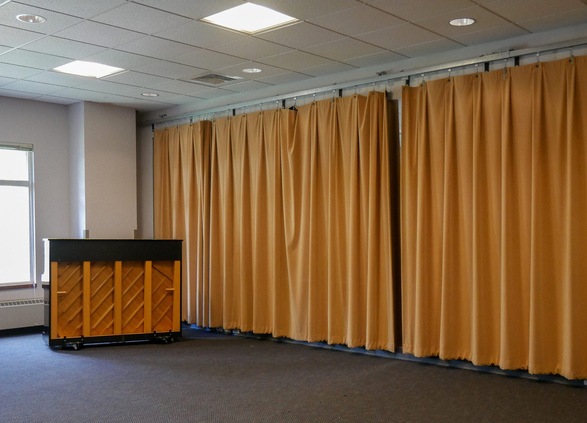 A large room with carpeted floors, a piano, and yellow curtains lining the wall.