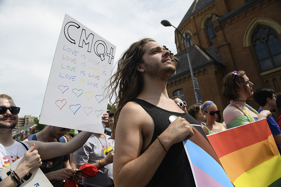 CMU students marching in the Downtown Pittsburgh Pride parade; one student with long brown hair wearing a black tank top and holding a pride flag is in the foreground.