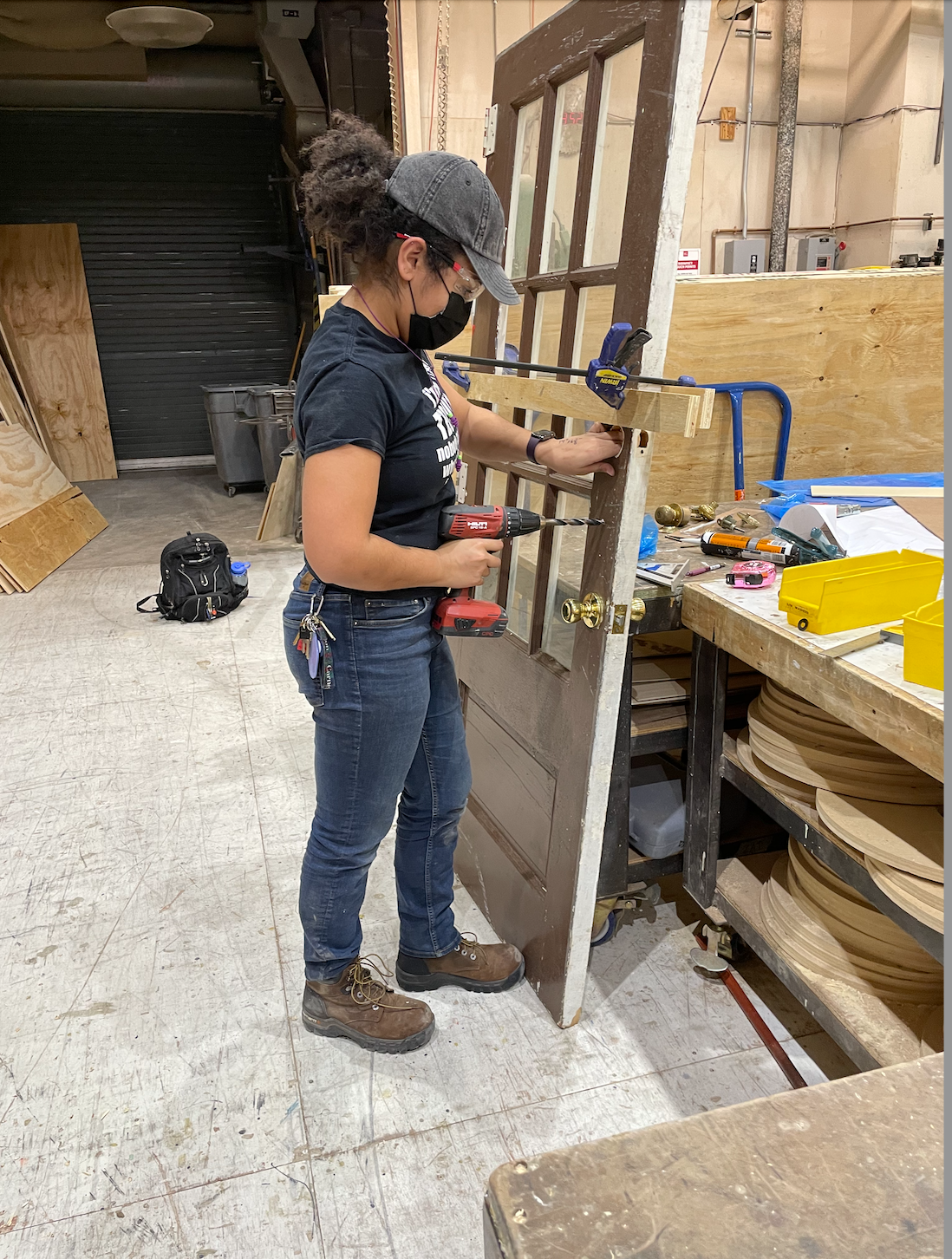 A student uses a drill on a set piece door in the School of Drama scene shop.