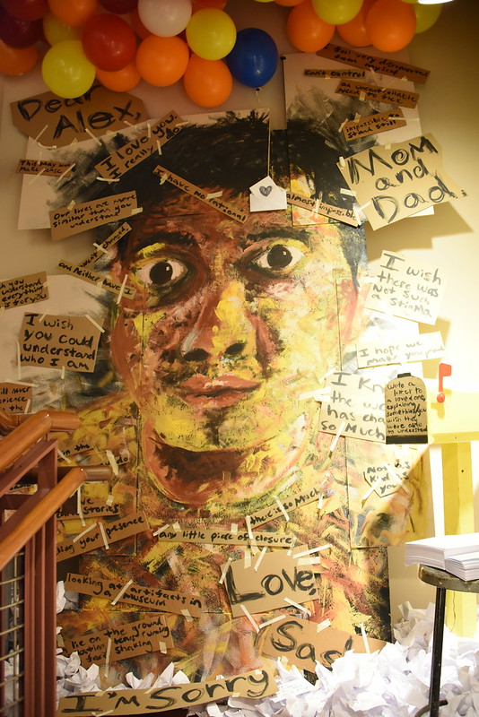 Wall of art that includes a large face, balloons, and handwritten notes.