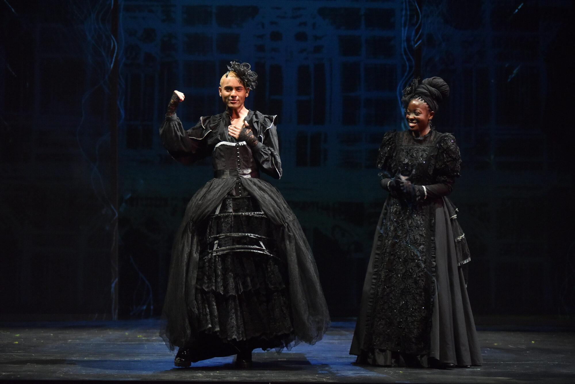 Two actors on stage, dressed in elaborate black Shakespearean costumes.