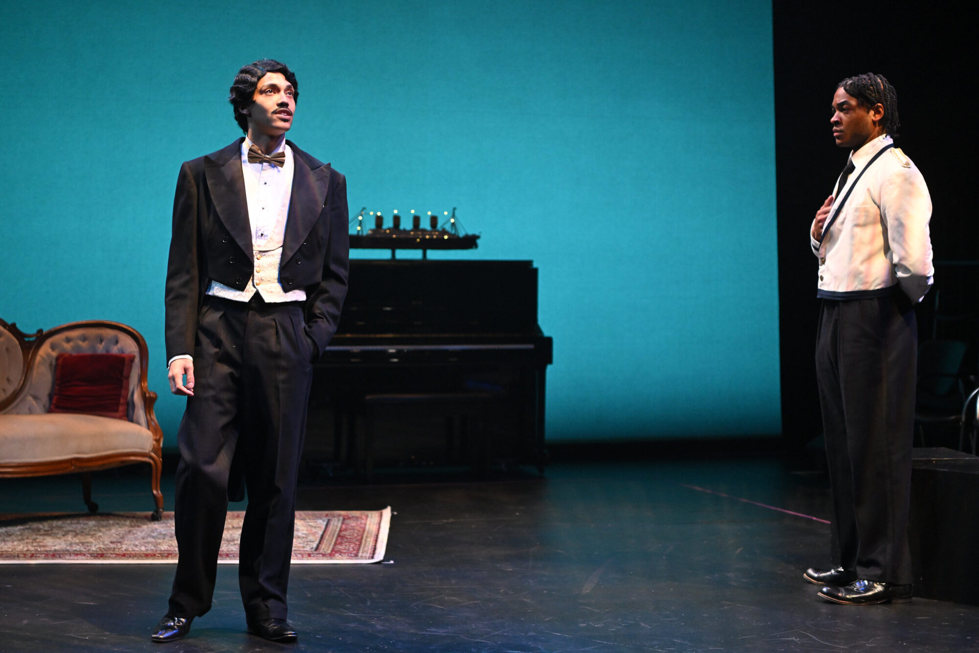 Two actors in suits stand on stage.