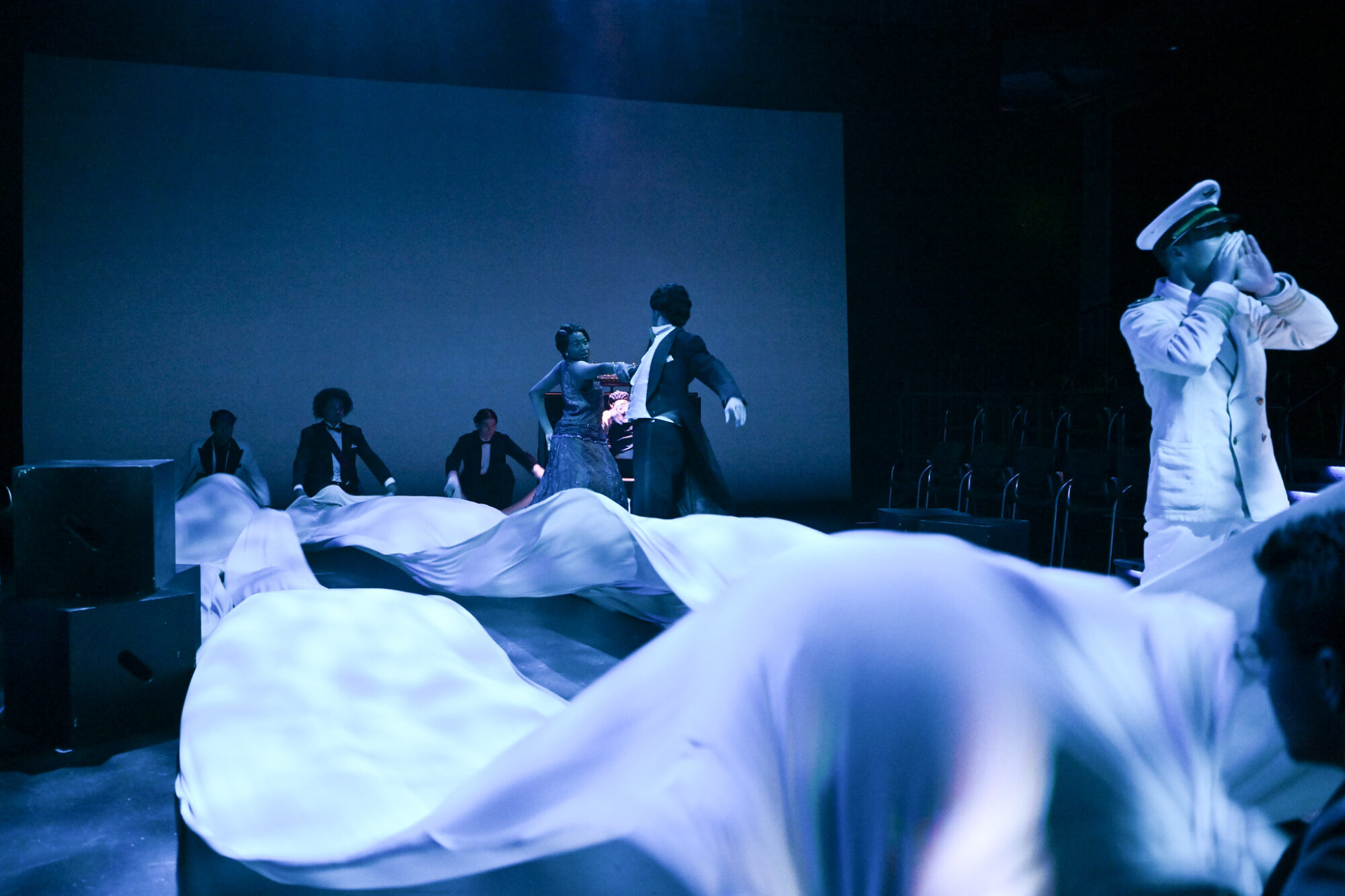 Actors in blue light with a white sheet waving over the ground in a scene from Twelfth Night.