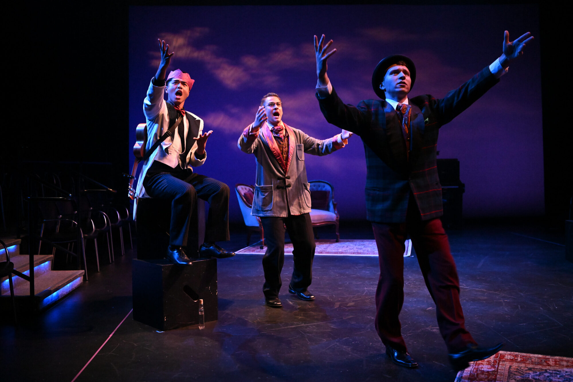 Three actors on stage, gesturing with their arms outstretched.