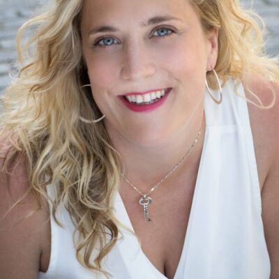 Jen Caprio, wearing a white sleeveless v-neck blouse smiles at the camera.