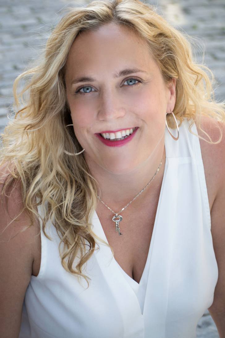 Jen Caprio, wearing a white sleeveless v-neck blouse smiles at the camera.