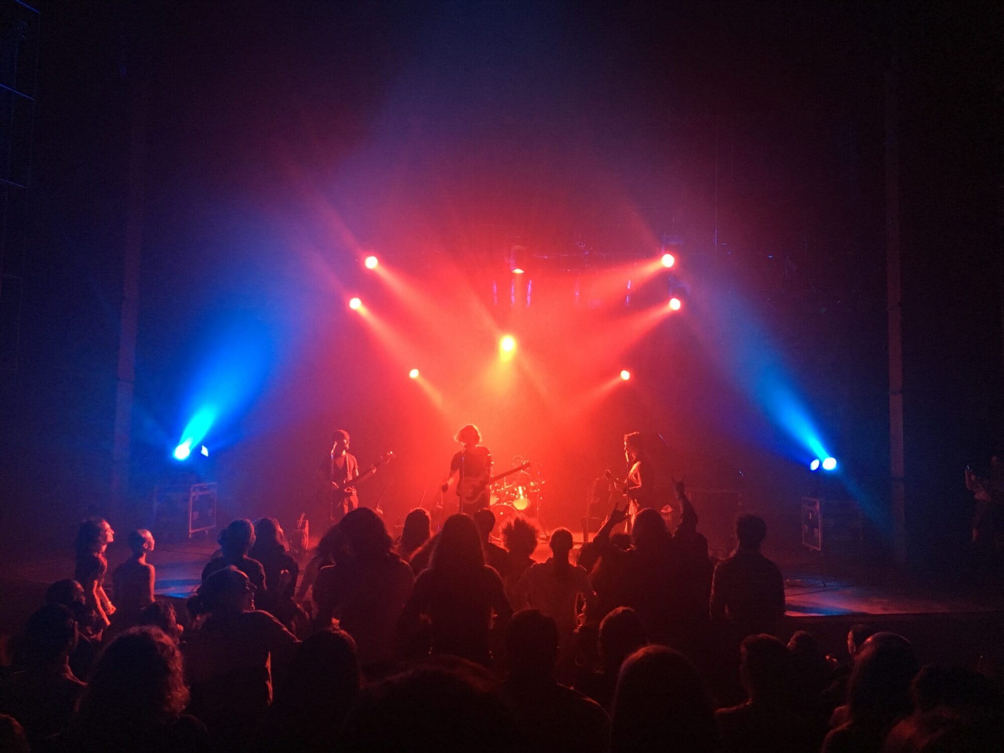 Photo of people watching a rock concert with red and blue lighting on the musicians on stage.