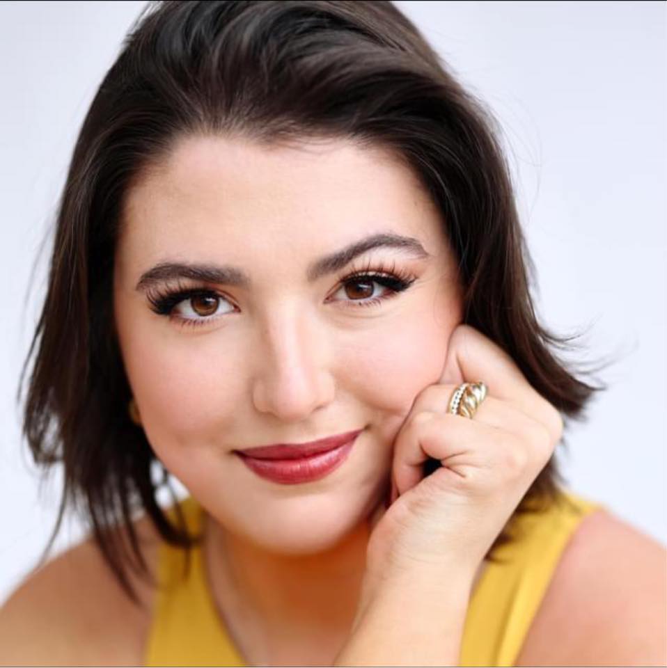 Headshot of Kaycee Swierc, a white woman with short dark hair, wearing a yellow sleeveless top and red lipstick.