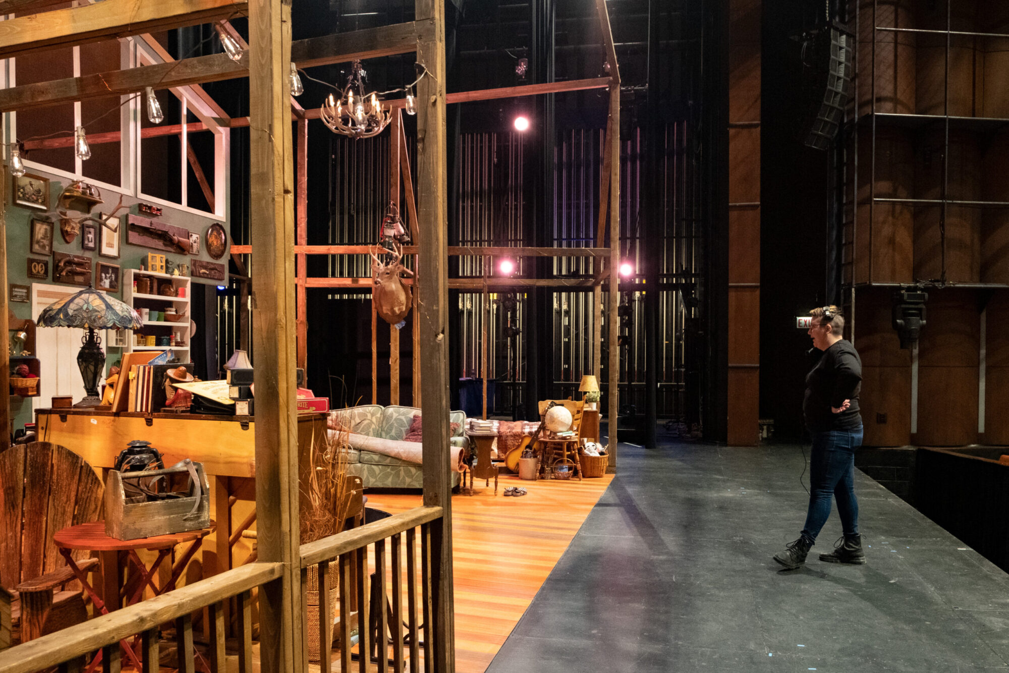 A student wearing all black and a headset stands on a set on stage in the Philip Chosky Theater.