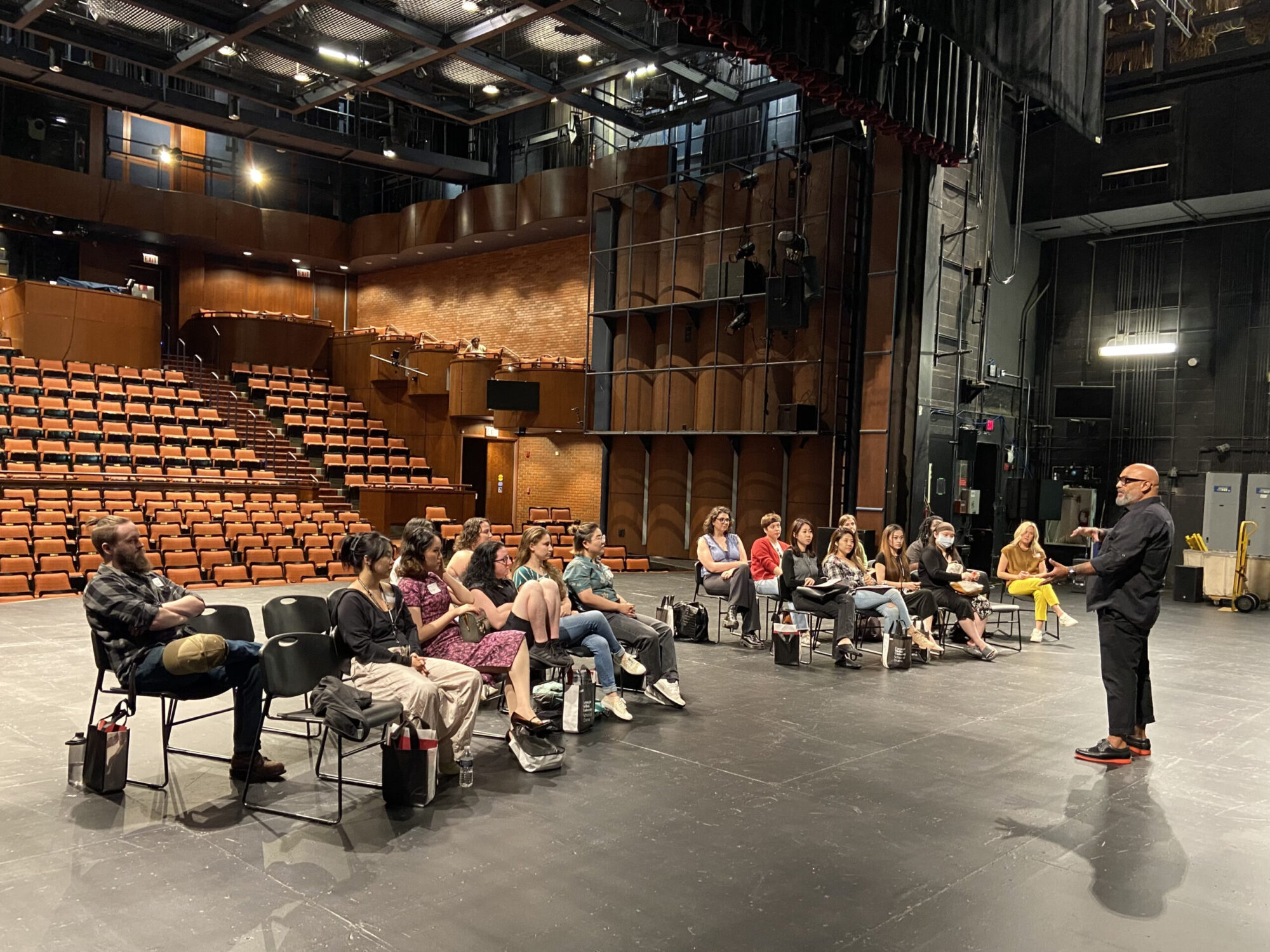 A group of students sits on chairs on the stage of the Chosky Theater, listens as Robert Ramirez speaks to them.