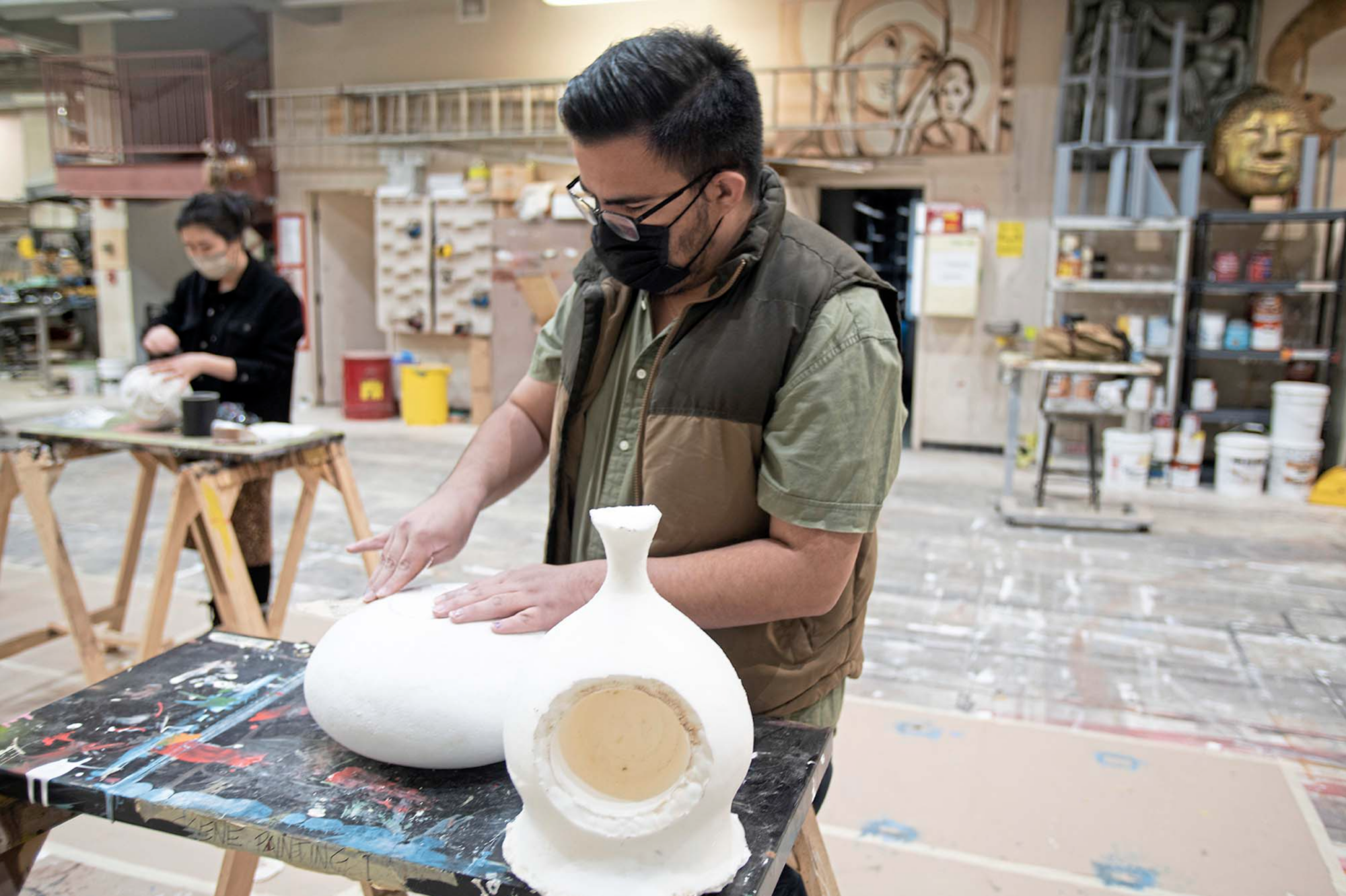 A student works on a white sculpture at a table in the scene shop at Carnegie Mellon.