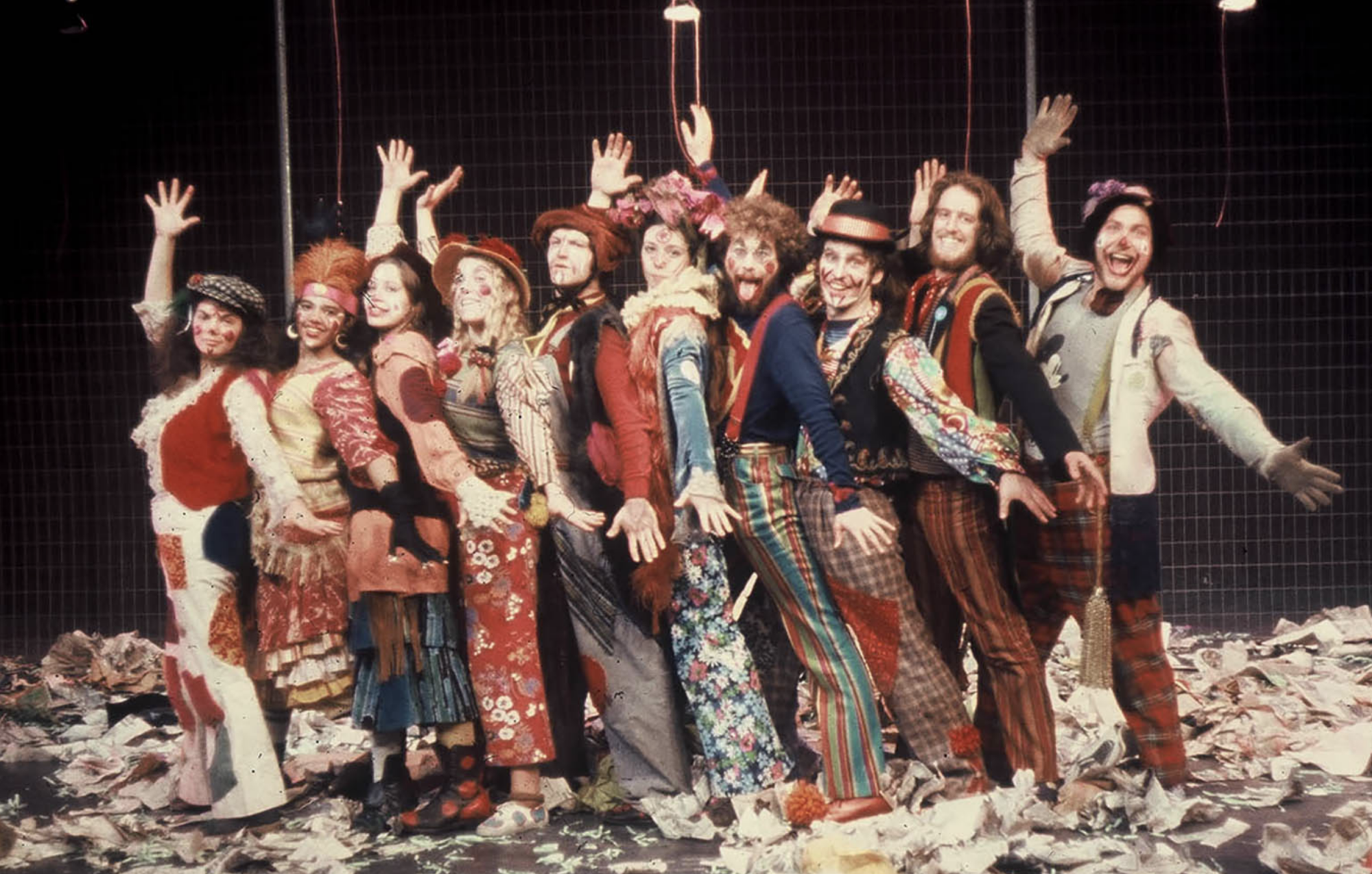 A group of 10 actors in costume stand in a line with arms outstretched in the first ever production of “Godspell” at Carnegie Mellon University.