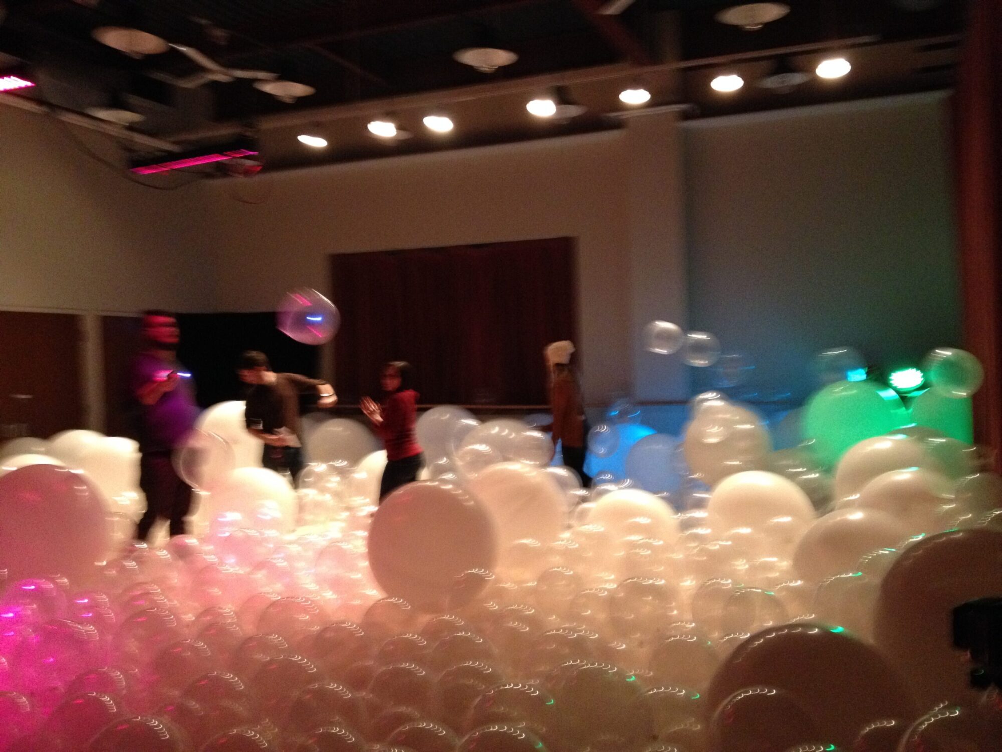 Photo of a room filled with white balloons and people playing with them.