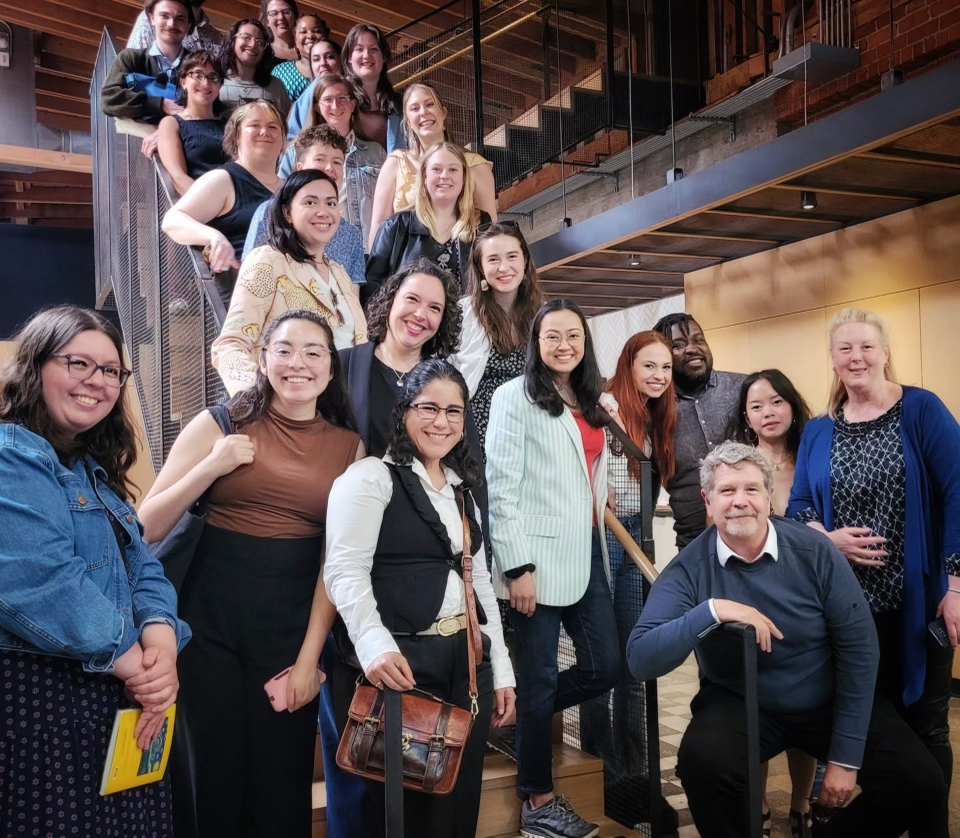 A group of students poses on a staircase with John Wells, crouching in front.