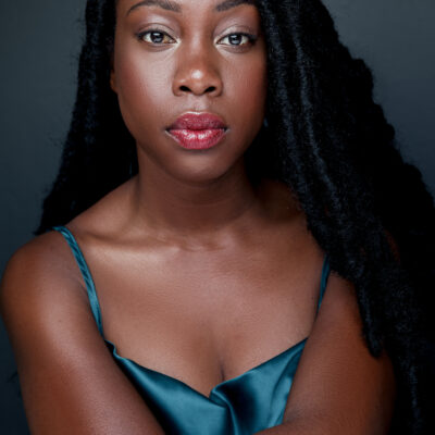 Photo of Alesia Etinoff, a Black woman with long dark hair, wearing a blue silk dress.