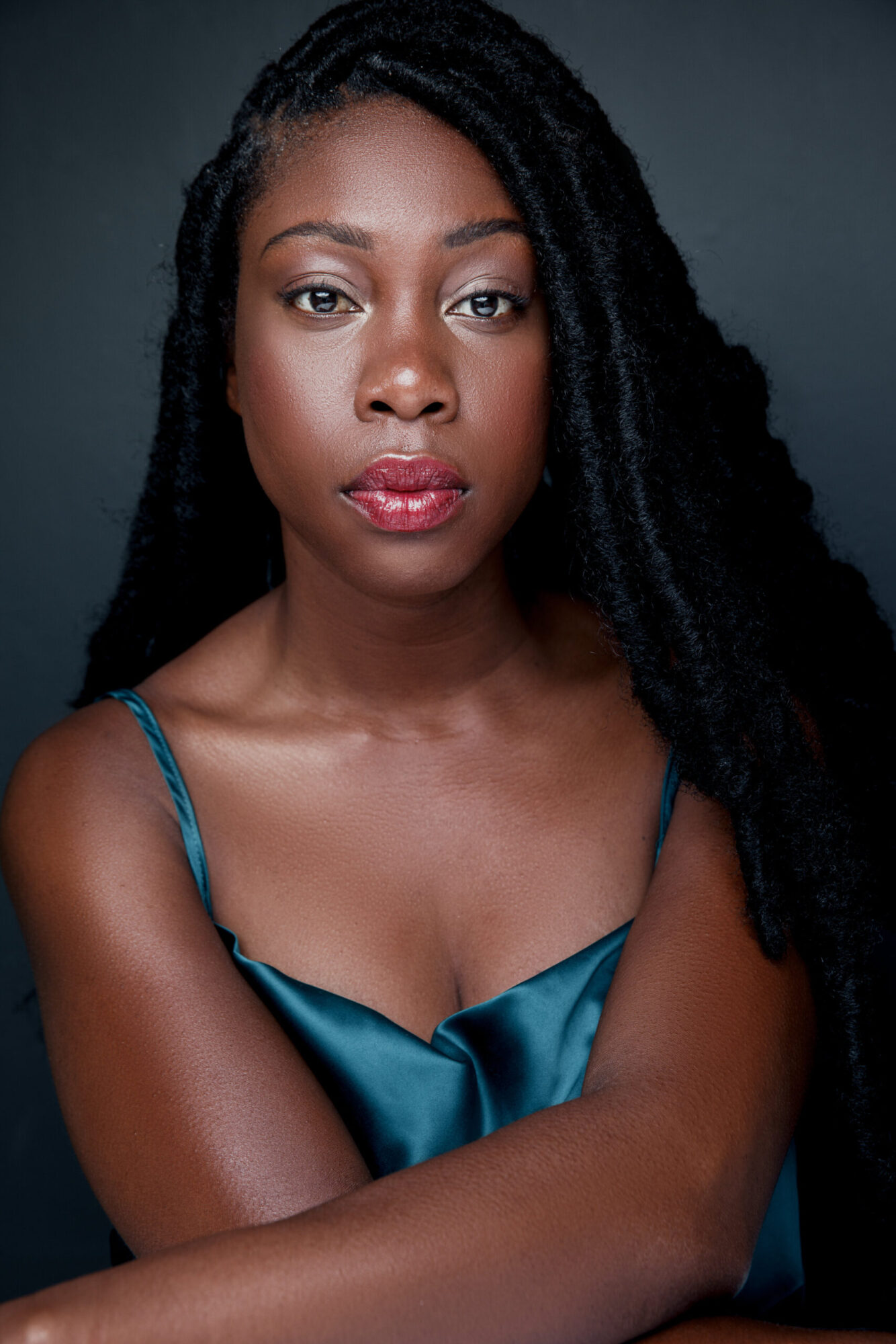 Photo of Alesia Etinoff, a Black woman with long dark hair, wearing a blue silk dress.