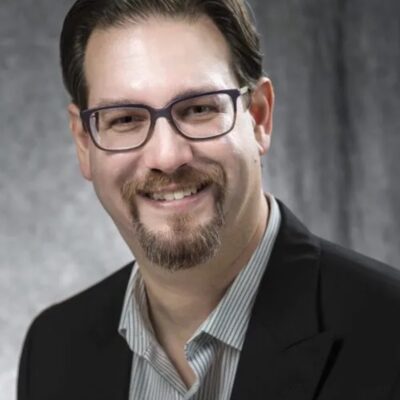 Photo of Brant Murray a white man with brown hair and glasses, wearing a collared shirt and suit jacket.