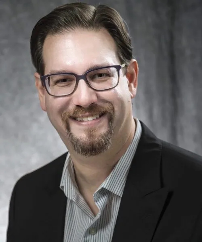 Photo of Brant Murray a white man with brown hair and glasses, wearing a collared shirt and suit jacket.