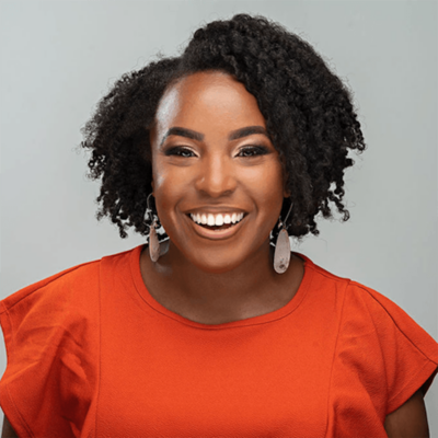 Photo of Brittany Thurman, a Black woman with short curly hair, wearing a brigh orange top and white earrings.