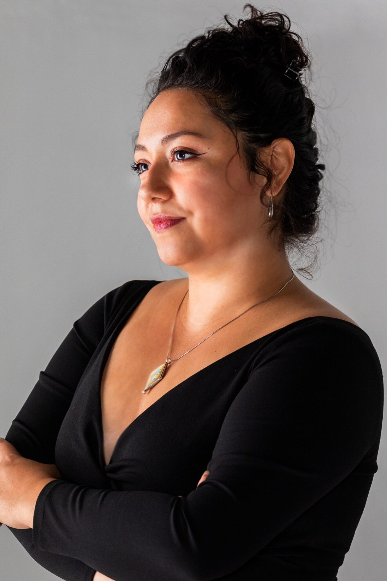 Photo of Carolyn Mazuca, a woman with dark hair pulled up, wearing a black v-neck blouse and necklace.