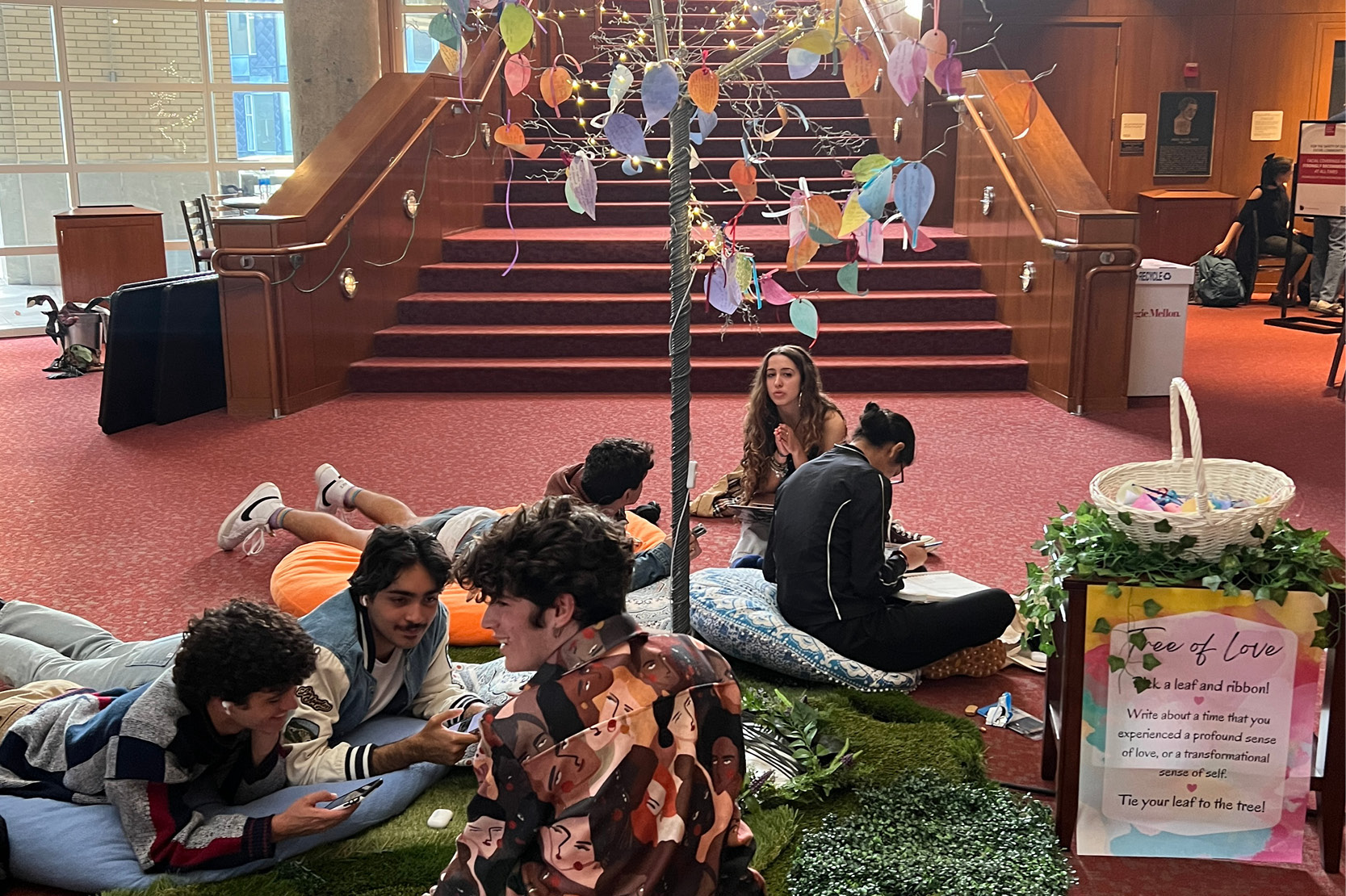 Students interact with a dramaturgy lobby display that is made up of colorful bean bags, a fake tree with colorful paper leaves, and twinkle lights.