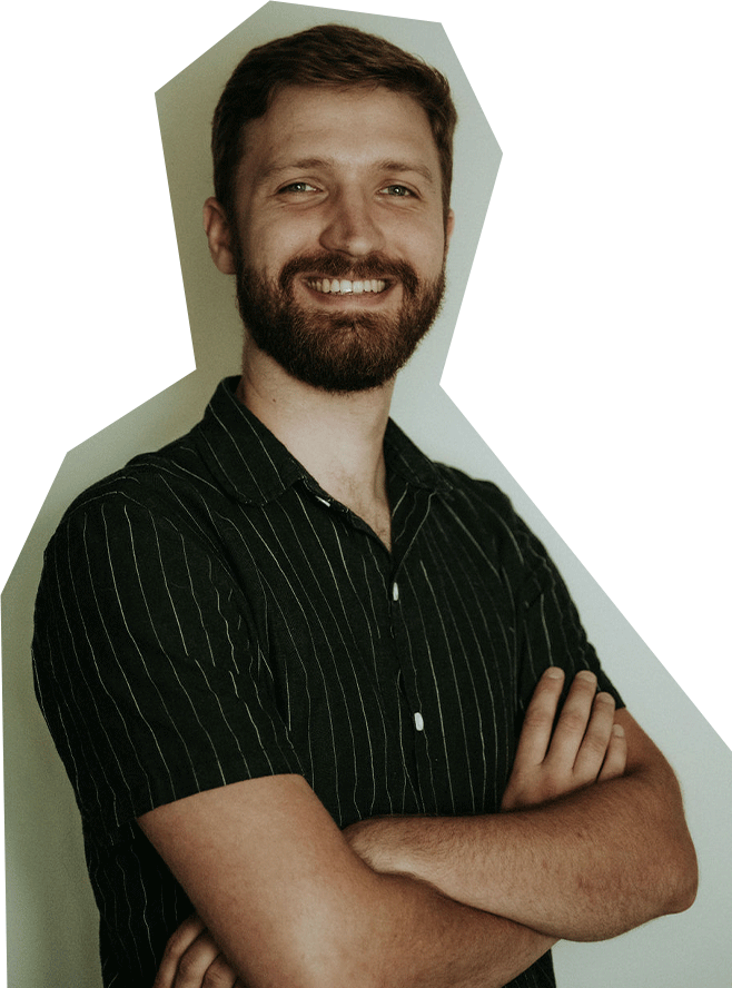 Photo of Thomas Feather, a white man with red/brown hair and beard, smiling and crossing his arms, wearing a short sleeved black buttoned shirt.