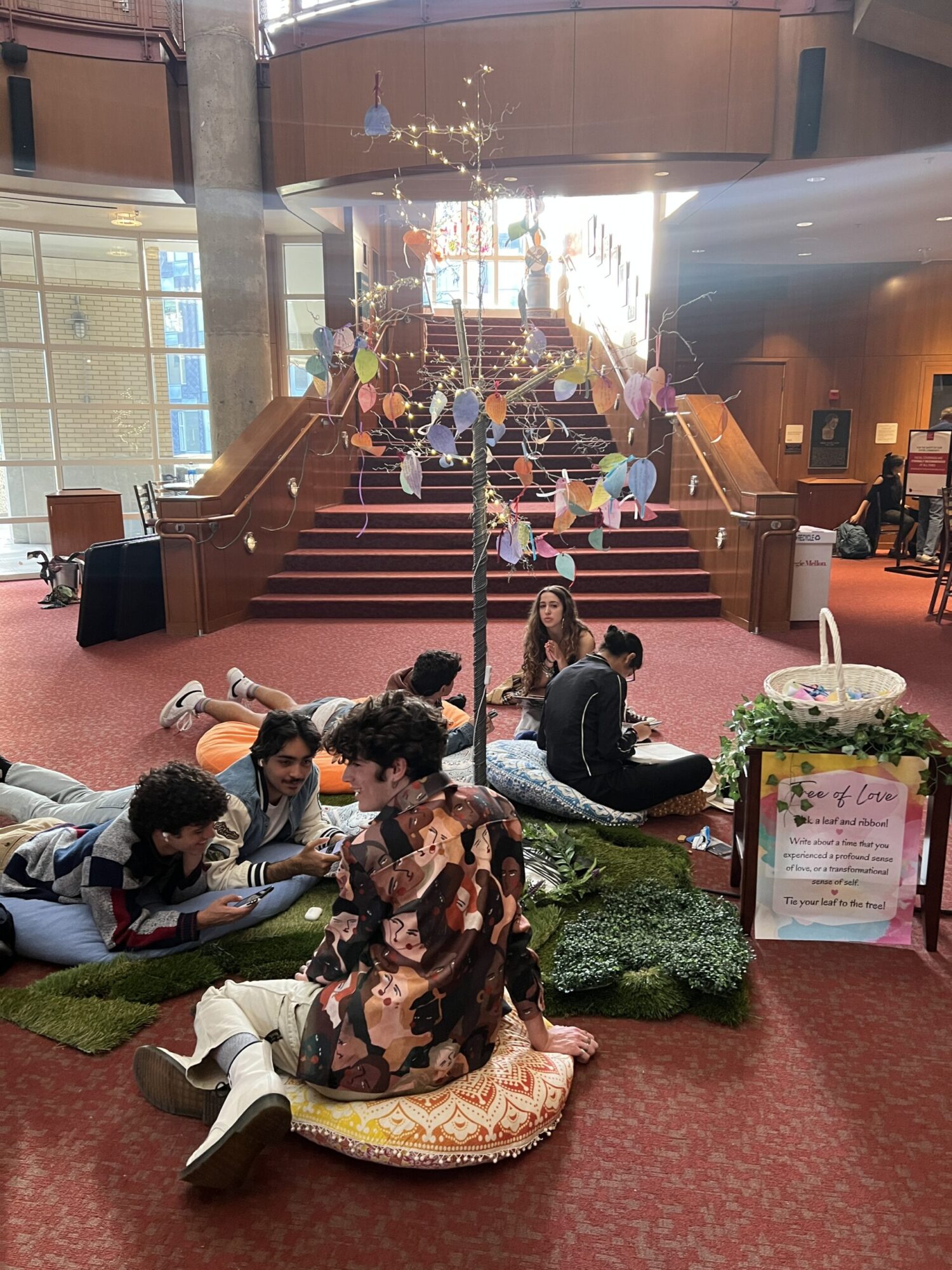 Students interact with a dramaturgy lobby display that is made up of colorful bean bags, a fake tree with colorful paper leaves, and twinkle lights.