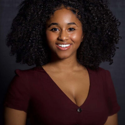 Photo of Jasmine Lesane, a Black woman with black curly hair wearing a maroon v-neck top.