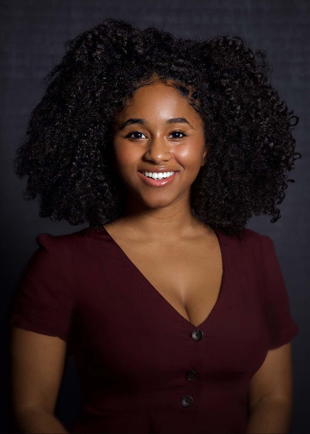 Photo of Jasmine Lesane, a Black woman with black curly hair wearing a maroon v-neck top.