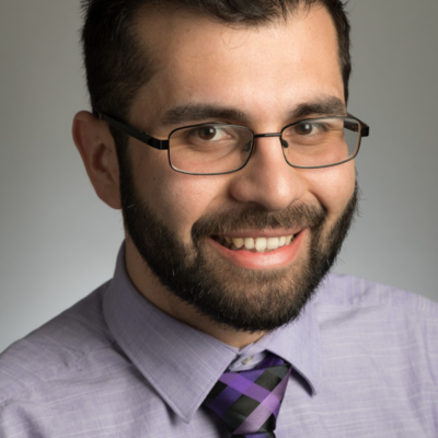 A photo of JuanCarlos Contreras, a man with dark brown hair and glasses wearing a shirt and tie.