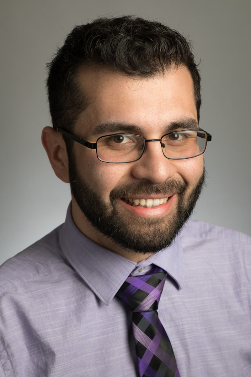 A photo of JuanCarlos Contreras, a man with dark brown hair and glasses wearing a shirt and tie.