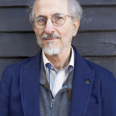 Photo of Jules Fisher, a white man with gray hair, white beard and glasses, wearing a collared shirt, gray zip-up, and navy blazer.