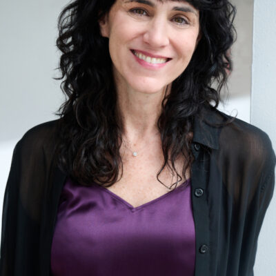 Photo of Leigh Silverman, a woman with long dark hair and bangs wearing a purple blouse and black cardigan.