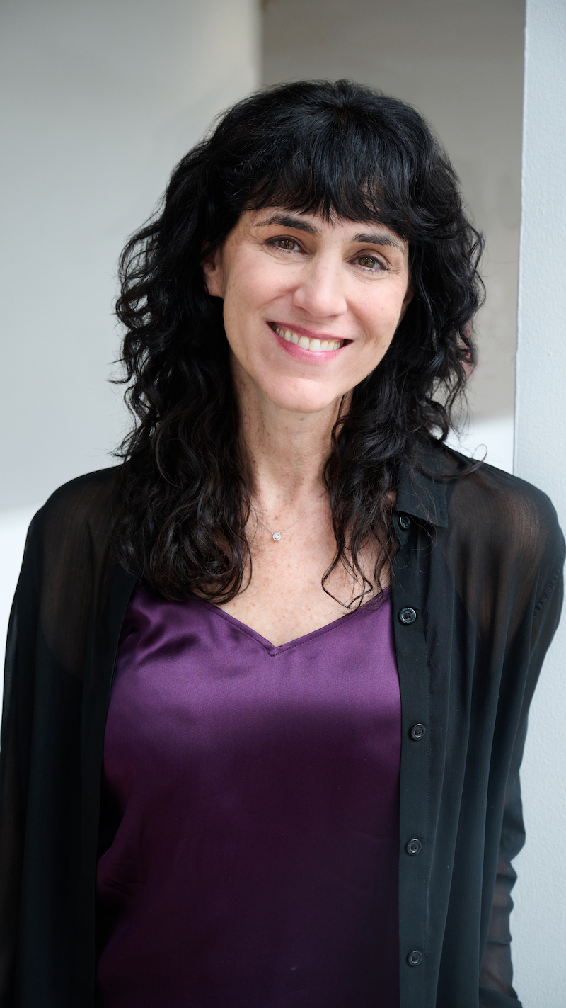 Photo of Leigh Silverman, a woman with long dark hair and bangs wearing a purple blouse and black cardigan.