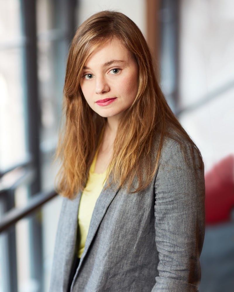 Photo of Liza Birkenmeier, a white woman with long blonde hair wearing a grey jacket over a pale yellow top.