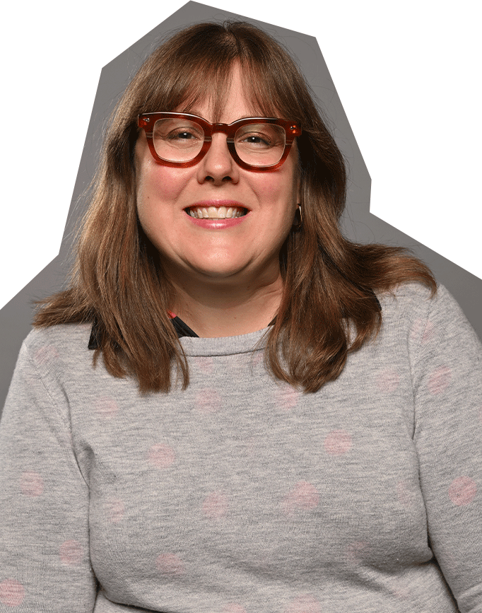 Photo of Sara Novelly, a white woman with medium length red/brown hair and red framed glasses, wearing a gray sweater.