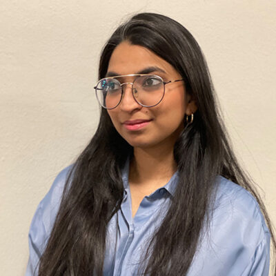 Photo of Oona Natesan, a woman with long dark hair wearing a blue button down blouse.